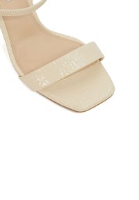 Beige patenten leren sandaal met een vierkante neus, twee brede banden en een dunne enkelband, met een gladde, glanzende textuur.