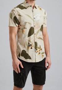 Kortærmet skjorte i beige stof med grøn og orange blomsterprint; har krave og knaplukning foran; parret med sorte cargo shorts.
