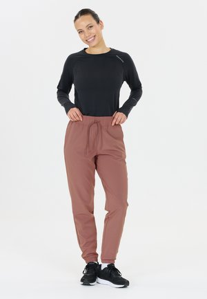 Zwarte sporttop met lange mouwen, gecombineerd met lichtbruine, taps toelopende joggingsbroeken met een elastische tailleband en koord. Zwarte sneakers maken de look compleet.