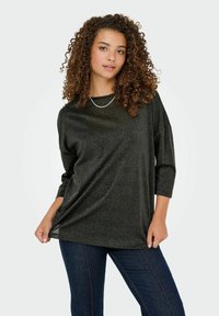 Sort top med afslappet pasform, trekvartærmer og en skinnende, struktureret overflade. Sammen med mørke denimjeans.