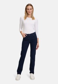 Jeans droit bleu marine en denim, avec une fermeture à bouton à l'avant, des passants de ceinture et des poches latérales, associés à un haut ajusté blanc.