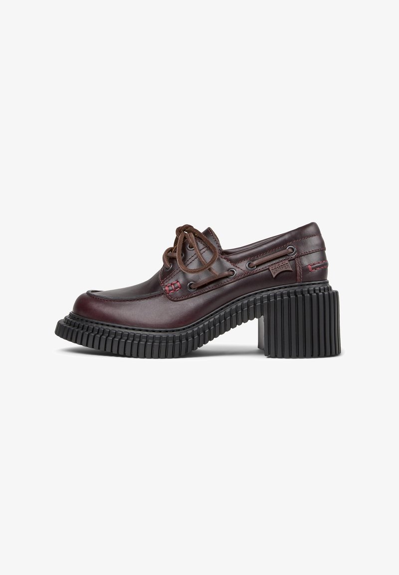 Brown leather shoe with a rounded toe and brown laces. Features a thick black ribbed heel and contrasting red stitching detail.