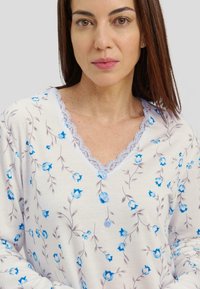 Blusa de manga larga con estampado floral en azul claro sobre un fondo crema, que presenta un escote en V con detalles de encaje y tres botones en el cuello.