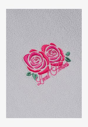 Polarowa tkanina w jasnoszarym tle z dwoma haftowanymi różowymi różami i zielonymi liśćmi, z napisem "Lokalni Bohaterowie".