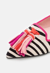 Chaussure plate à bout pointu avec des rayures noires et blanches, une bordure rose et des glands en daim rose, rouge et magenta sur le devant.
