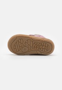 Chaussure d'enfants rose avec une semelle en caoutchouc, dotée d'un fond texturé, d'une doublure douce et d'une lanière Velcro. Logo remarquable embossé à l'arrière.