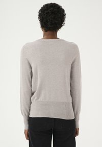 Pull gris clair avec un col rond, des poignets et un ourlet côtelés, fabriqué en maille douce, porté sur un jean noir.