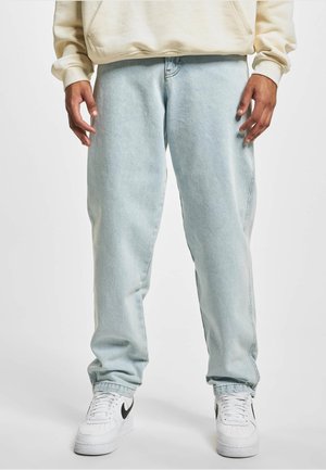 Lysblå denimjeans med en afslappet pasform, der har sidesømme og en let tilspidset ankel, båret med hvide sneakers.