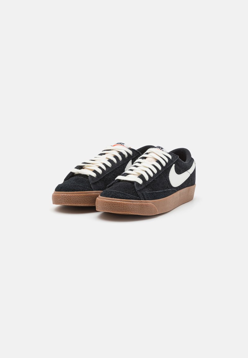 Zapatillas de ante negro con acentos y cordones blancos, que presentan una suela de goma marrón texturizada y un diseño de perfil bajo.