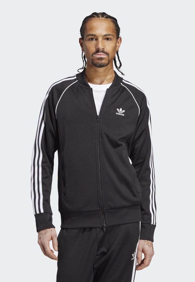 Melna sporta jaka ar rāvējslēdzēju, ar baltām trīs svītru akcentiem uz piedurknēm un Adidas logo uz krūšu daļas. Mīksta tekstūra, pieguloša forma.