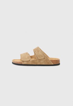 Suede sandály v světlé béžové barvě s dvěma nastavitelnými suchými zipy, korkovou stélkou a texturovanou černou gumovou podrážkou. Plný design, otevřená špička.