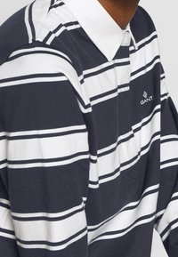 Navy- und weißgestreiftes Langarm-Polohemd mit Button-Down-Kragen. Verfügt über ein kleines Logo auf der Brust und ein texturiertes Gewebe.