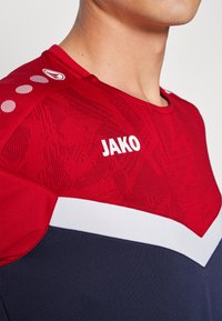 Rode sportshirt met een textuurpatroon, witte streep en logo met ronde accenten op de schouder. Glad stof, ronde halsontwerp.