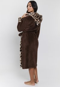 Bata de felpa marrón con capucha de estampado de leopardo. Presenta un cinturón de lazo y una textura suave. Termina justo por encima de los tobillos.
