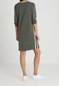 Robe à manches courtes de couleur vert olive avec une coupe droite, des bandes blanches sur les côtés et un col arrondi. Portée avec des baskets blanches.