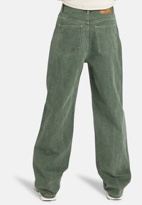 Jean large vert avec une texture délavée, présentant des poches arrière doubles, des passants de ceinture et des coutures contrastées.