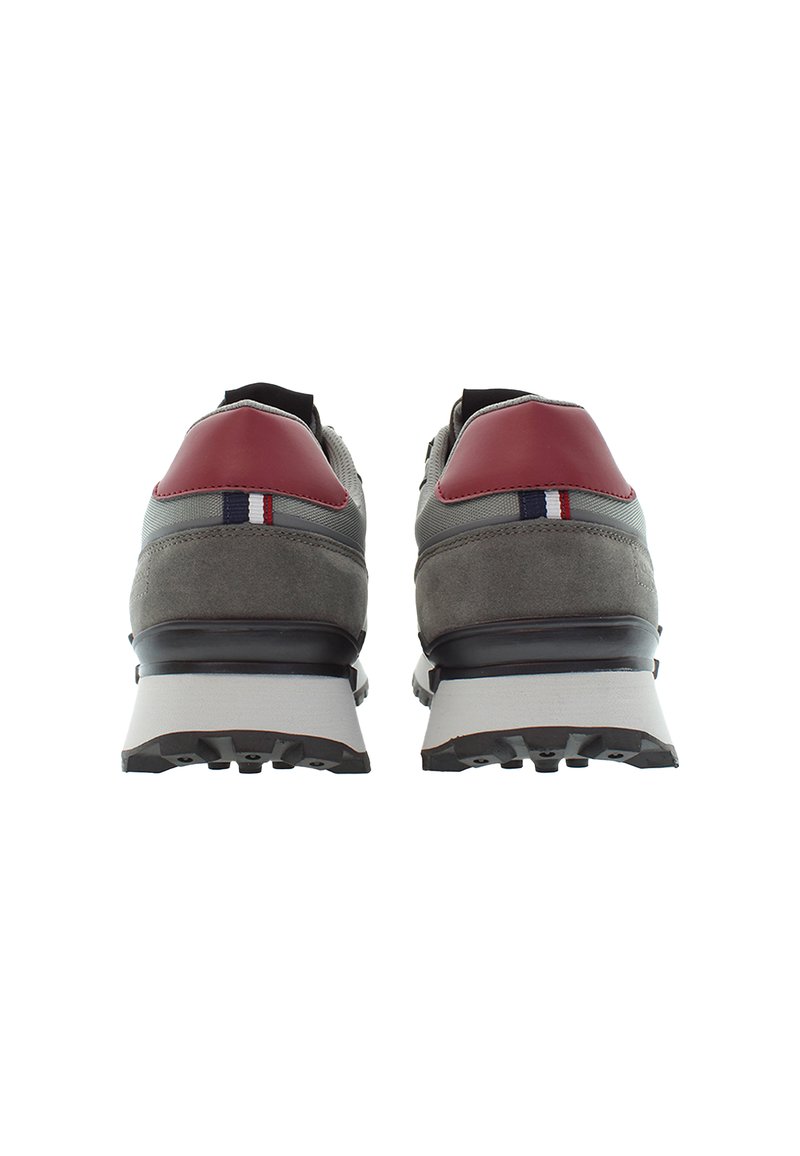 Un paio di sneakers grigie con accenti rossi sul tallone e suole bianche, viste da dietro su uno sfondo bianco.