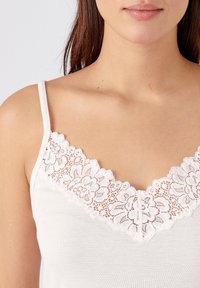 Top de tirantes blanco con delicado encaje floral en el escote. Tirantes ajustables y tela suave y texturizada. Diseño simple y elegante.