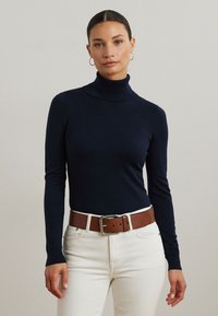 Marinefarbener Rollkragenpullover aus weichem Material, kombiniert mit hochgeschnittenen weißen Jeans und einem braunen Gürtel mit einer silbernen Schnalle.