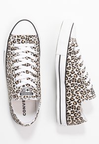 Sapatilhas de lona com estampa de leopardo, atacadores brancos, bico de borracha e acabamento preto. Apresenta um logo na língua e sola texturada.