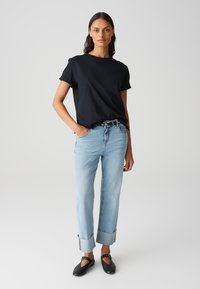 T-shirt nera in cotone con maniche arrotolate, jeans dritti blu chiaro con orli risvolti e scarpe nere basse. Design semplice e casual.