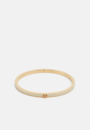 Brățară din metal cu finisaj auriu, cu o suprafață netedă și lustruită. Prezintă un design îngust și un accent decorativ central cu un logo.