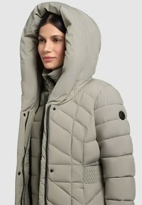 Puffy quilted jacket in light gray, featuring a large hood, zip closure, and side pockets, with a textured panel on the sides.