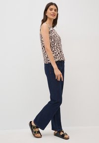 Mouwloos topje in crème met donkerpaarse luipaardprint, gecombineerd met donkerblauwe rechtlijnige jeans en zwarte sandalen met gespdetails.