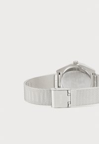 Srebrny zegarek na siateczkowym pasku z geometr case. Posiada polerowaną srebrną klamrę oraz minimalistyczny design. Gładka powierzchnia i czyste linie.