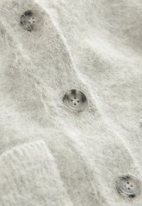 Light gray cardigan made of soft, fuzzy material, featuring large, round, gray buttons and ribbed accents. Textured, cozy look.