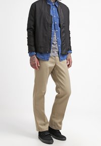 Sort bomberjakke over en blå denimskjorte, lys grå stribet T-shirt, beige bukser og sorte sneakers. Funktioner: glat tekstur, afslappet pasform.