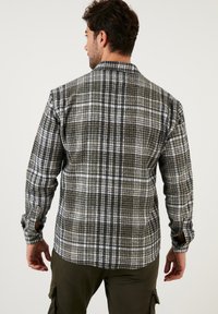 Kockás flanelingat, amely sötétzöld, tengerészkék és fehér színek keverékéből készült. Hosszú ujjú, gombos mandzsettával és klasszikus gallér kialakítással.