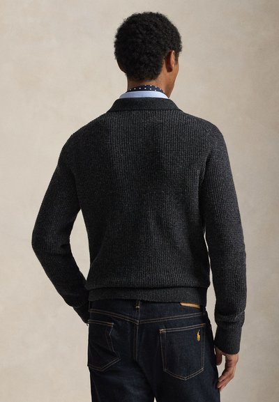 Dark gray knit sweater with a textured surface, featuring a mock collar and long sleeves, paired with dark jeans. Simple, fitted design.