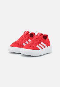 Røde strikkede slip-on sko med hvite detaljer, som har tre hvite striper og en polstret hvit såle. Teksturert overdel for fleksibilitet.