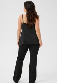 Čierny top na tenkých ramienkach so hladkou, plynulou textúrou, skombinovaný s čiernymi širokými nohavicami, vytvára harmonický vzhľad outfitu.