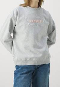 Sudadera gris de algodón con cuello redondo, que presenta un logo de Levi's bordado en rosa claro en el pecho. Ajuste casual.