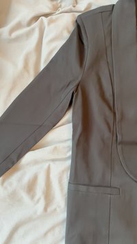 Blazer cinza feito de um tecido suave, com um colarinho elegante, fecho de um único botão, silhueta aerodinâmica e um bolso lateral.