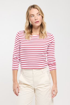Chemise à manches longues rayée rouge et blanche, avec un col rond. Associée à un pantalon crème, mettant en valeur une coupe ajustée.