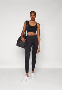 Črni športni modrček in gamaše z visokim pasom, združeni z belimi supergami in črno športno torbo, vsi z elegantno, minimalistično zasnovo.