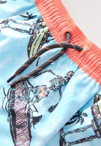 Blue swim shorts with a coral waistband, featuring a skeleton print and textured drawstring. Contains tropical-themed accents.