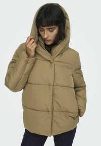Polstrovaná hnědá bunda s kapucí a zipem, s vodorovným švem a postranními kapsami, v kombinaci s tmavými džíny.