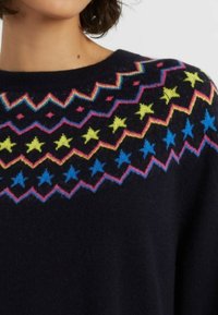 Zwarte gebreide trui met een multikleurig geometrisch patroon met roze, gele en blauwe sterren langs de halslijn en schouderpartij.