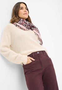 Pullover beige in maglia abbinato a pantaloni bordeaux. Una sciarpa a fantasia presenta colori rosa, nero e bianco, posata attorno al collo.