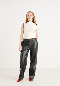 White sleeveless top with a black neckline, paired with black faux leather wide-leg pants and red pointed-toe shoes. Simple background.