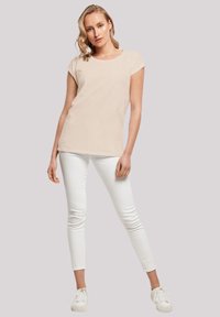Beige short-sleeve t-shirt with a round neckline, paired with white skinny jeans and white sneakers. Smooth fabric, casual fit.