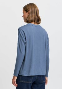 Blå ribbad långärmad topp med rund hals och sjunkna axlar, ihop med mörk denimbyxor. Texturen är mjuk och avslappnad.