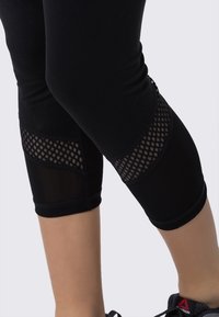 Černé sportovní legíny s síťovinovými panely na kolenou, přiléhavý design a zkrácená délka. Ozdobené texturovaným vzorem.