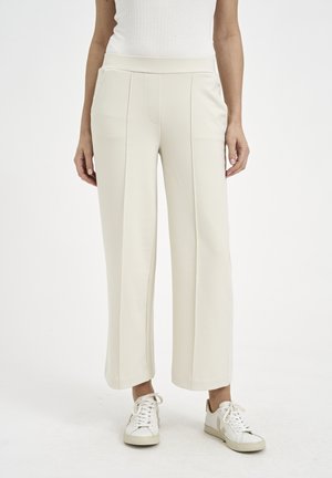 Beige wide-leg pants made of soft fabric, featuring a smooth waistband and front pleats, paired with white sneakers.