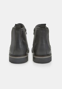 Stivali neri in pelle alla caviglia con chiusura a zip sul retro, texture liscia, punta tonda e suola in gomma robusta. Dettaglio di cuciture decorative.