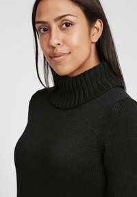 Schwarzer gestrickter Pullover mit hohem Rippenkragen, der einen strukturierten Stoff und ein figurbetontes Design präsentiert und Wärme sowie Komfort betont.